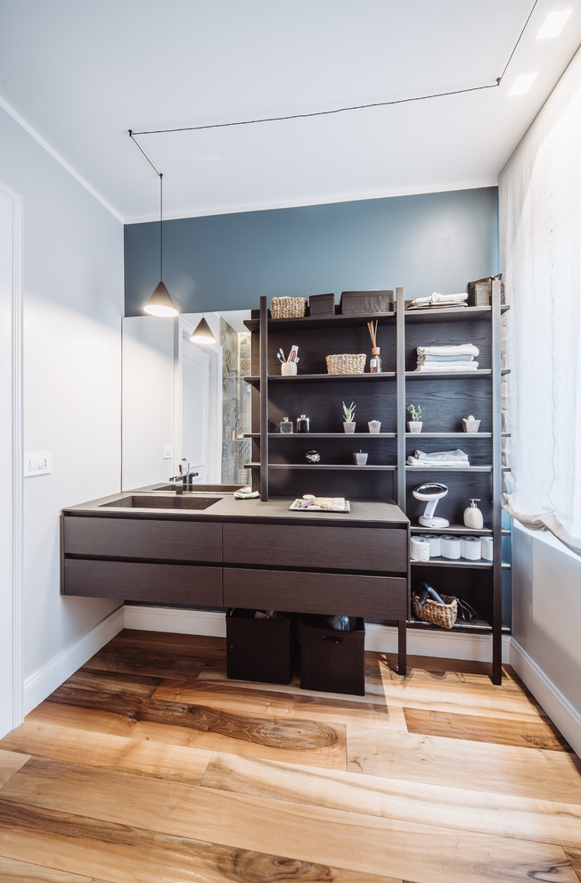 This is an example of a contemporary bathroom in Turin with dark wood cabinets, blue walls, medium hardwood floors, an integrated sink, brown floor, brown benchtops and flat-panel cabinets.