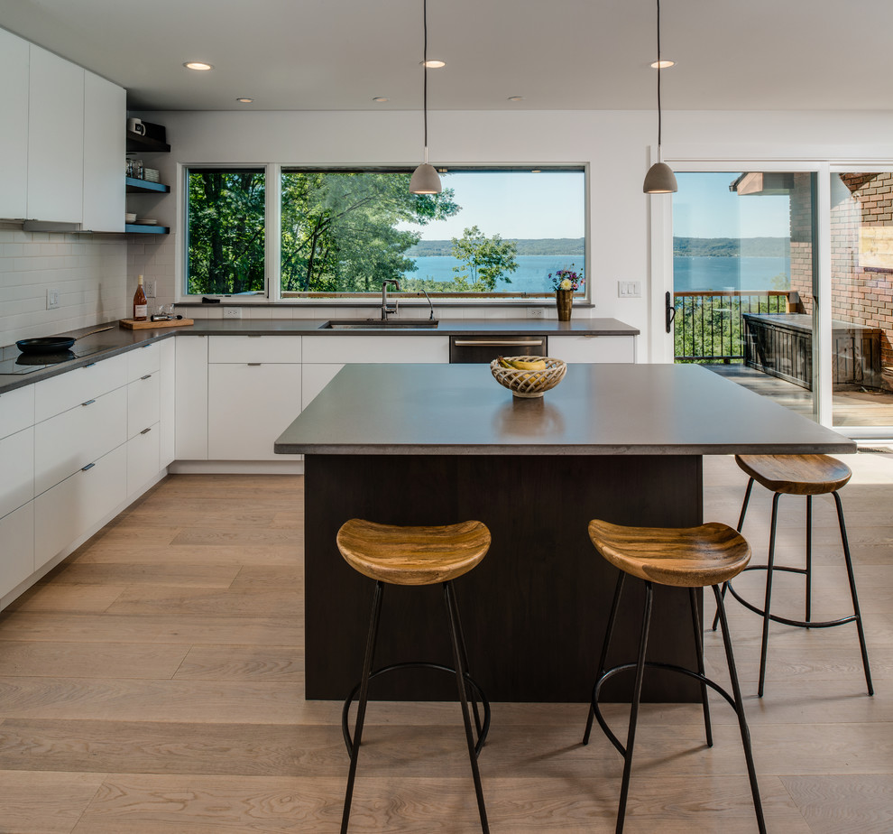 Photo of a mid-sized contemporary l-shaped kitchen in Other with an undermount sink, flat-panel cabinets, white cabinets, concrete benchtops, white splashback, ceramic splashback, stainless steel appliances, light hardwood floors and with island.