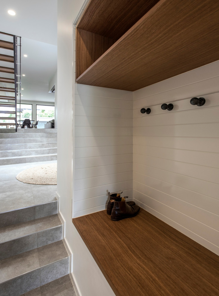 This is an example of a contemporary mudroom with white walls, ceramic floors, a pivot front door and grey floor.