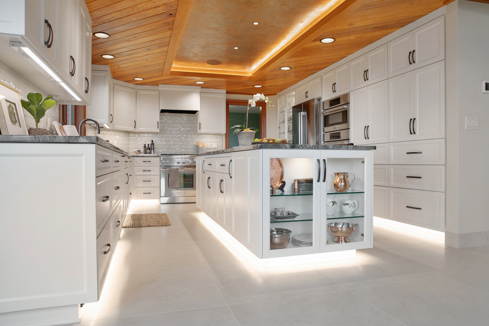 This is an example of a large transitional u-shaped eat-in kitchen in Portland with an undermount sink, recessed-panel cabinets, white cabinets, quartzite benchtops, white splashback, glass tile splashback, stainless steel appliances, porcelain floors, with island, beige floor, grey benchtop and recessed.