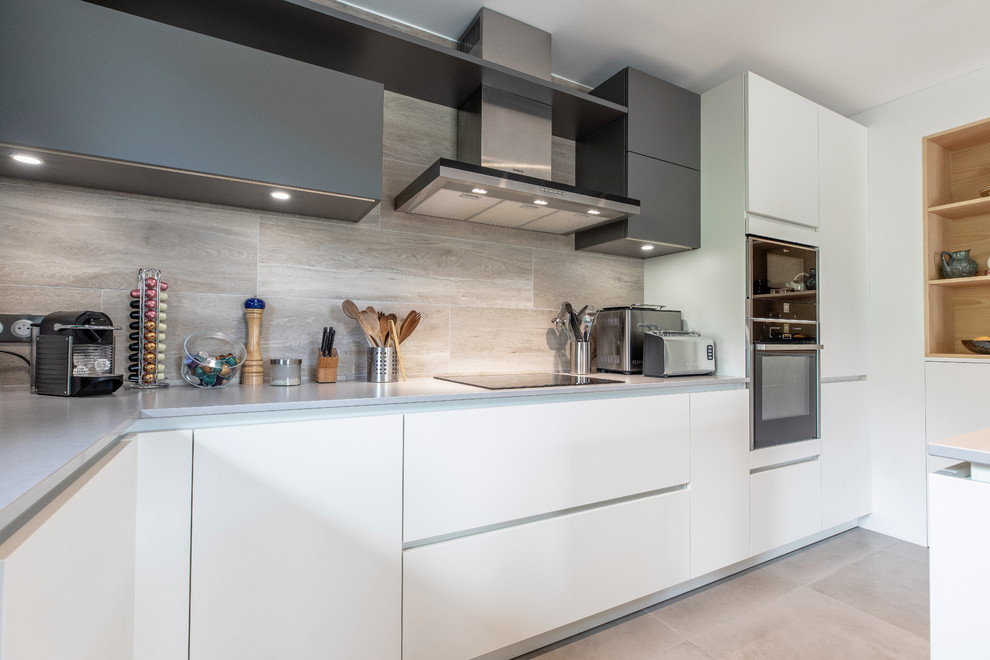 This is an example of a mid-sized modern u-shaped open plan kitchen in Grenoble with a single-bowl sink, white cabinets, quartzite benchtops, with island, grey benchtop, flat-panel cabinets, beige splashback, stainless steel appliances, ceramic floors and beige floor.