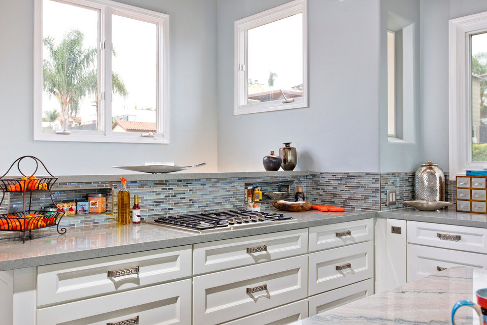 This is an example of a large beach style u-shaped open plan kitchen in San Diego with a farmhouse sink, recessed-panel cabinets, white cabinets, quartzite benchtops, blue splashback, glass tile splashback, stainless steel appliances, dark hardwood floors and with island.