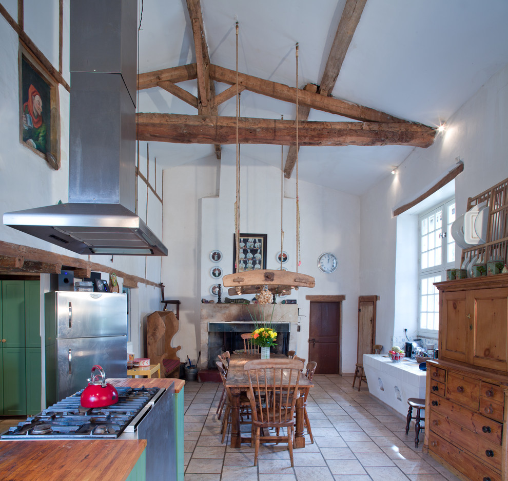 This is an example of a country eat-in kitchen in London with wood benchtops, green cabinets and stainless steel appliances.