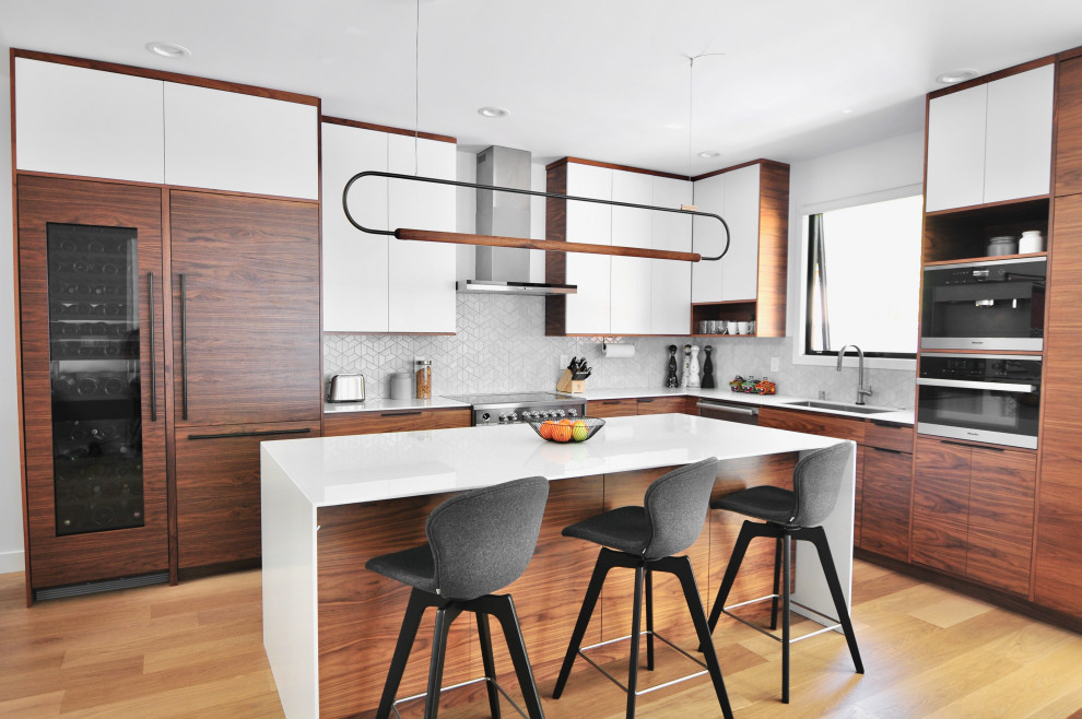 Midcentury l-shaped kitchen in San Francisco with an undermount sink, flat-panel cabinets, medium wood cabinets, white splashback, panelled appliances, light hardwood floors, with island, beige floor and white benchtop.