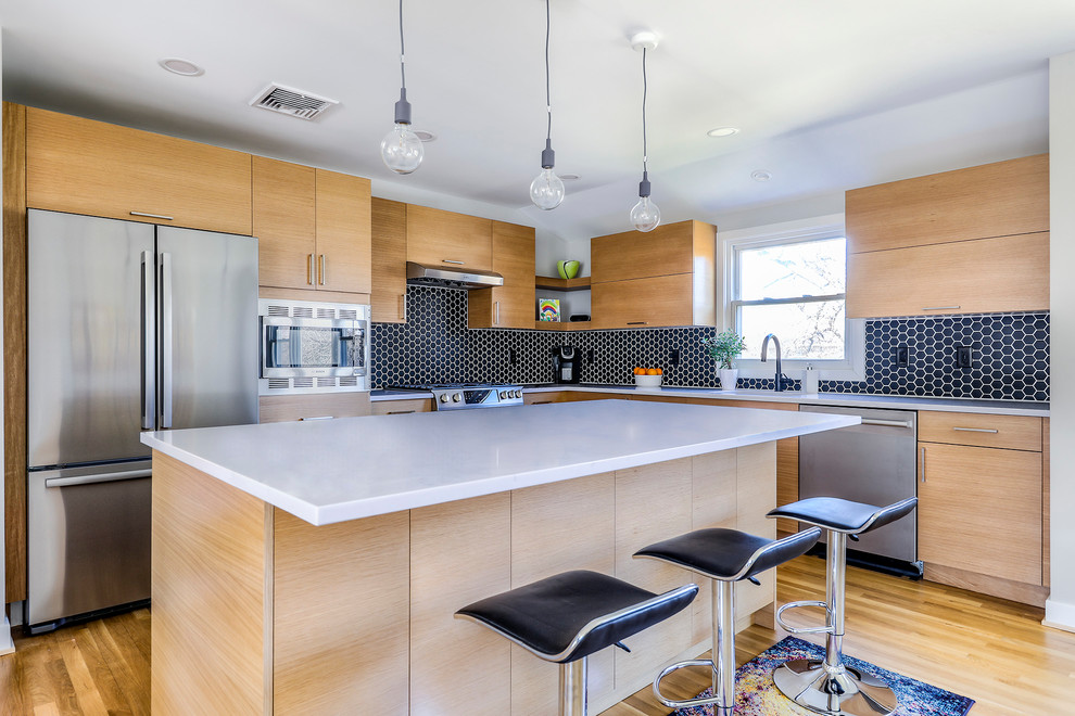 Photo of a mid-sized contemporary l-shaped kitchen in New York with flat-panel cabinets, light wood cabinets, quartzite benchtops, black splashback, porcelain splashback, stainless steel appliances, light hardwood floors, with island, white benchtop and beige floor.