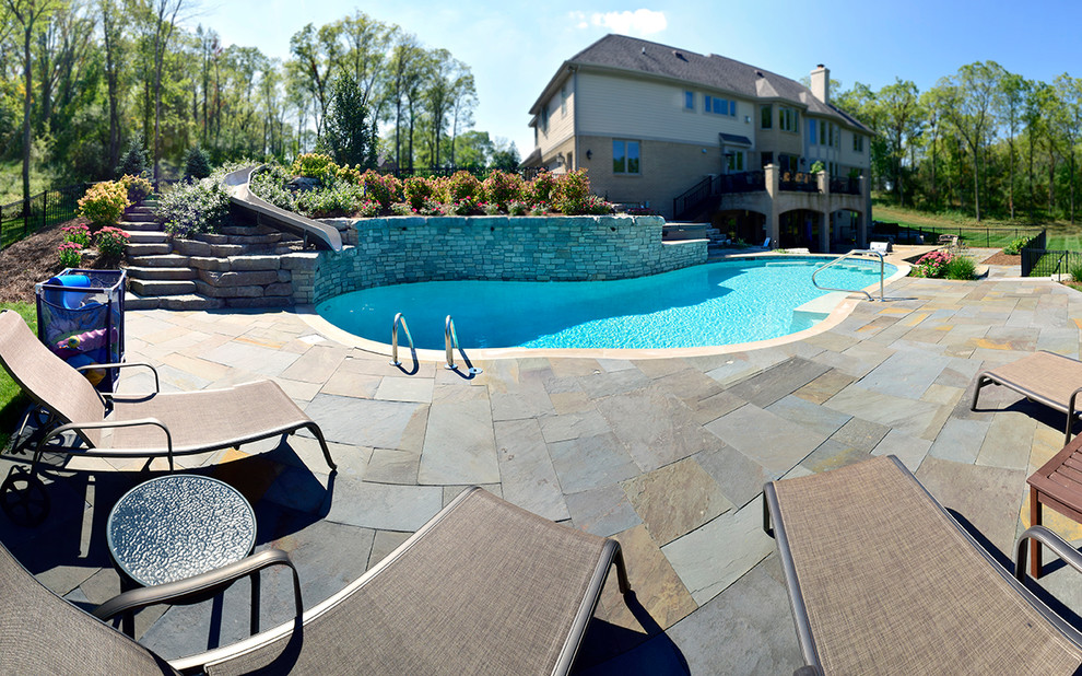 This is an example of a large transitional backyard custom-shaped pool in Detroit with a water slide and natural stone pavers.