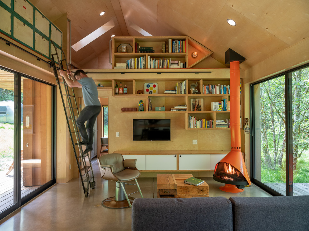 Ejemplo de sala de estar con biblioteca tipo loft rústica pequeña con suelo de cemento, estufa de leña, televisor colgado en la pared, suelo gris, madera y madera