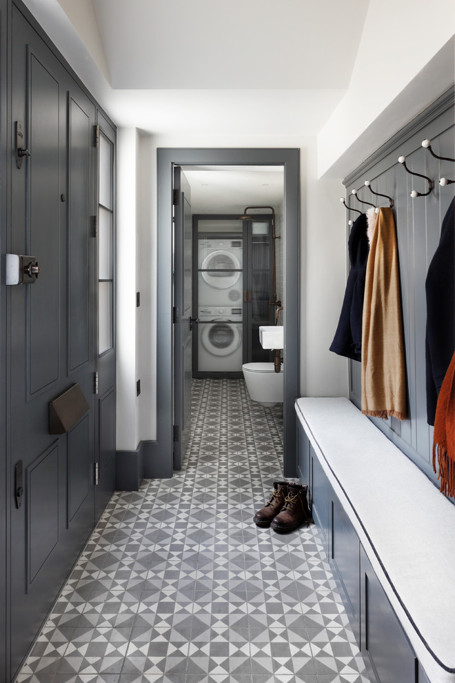 This is an example of a mid-sized contemporary galley utility room in London with an utility sink, open cabinets, blue cabinets, white walls, ceramic floors, a stacked washer and dryer, grey floor and white benchtop.