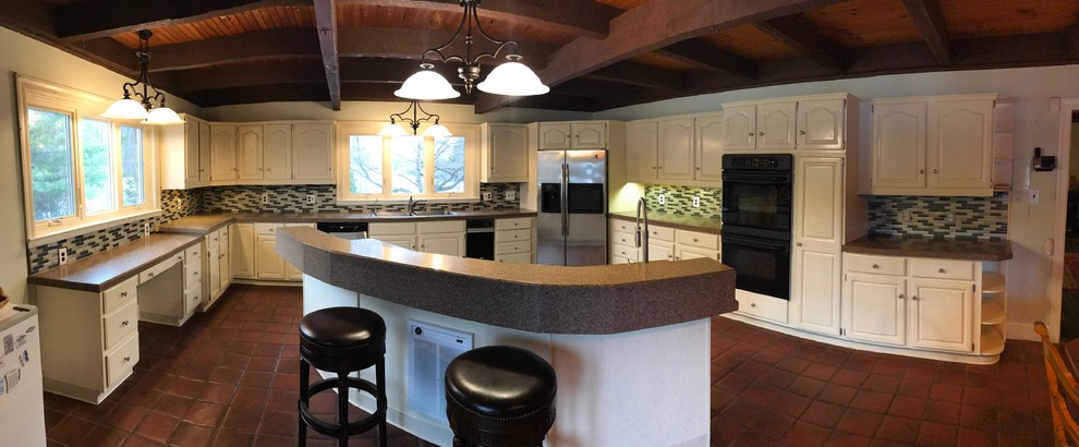Large country u-shaped kitchen pantry in Philadelphia with a double-bowl sink, raised-panel cabinets, white cabinets, granite benchtops, metallic splashback, glass tile splashback, stainless steel appliances, terra-cotta floors and with island.