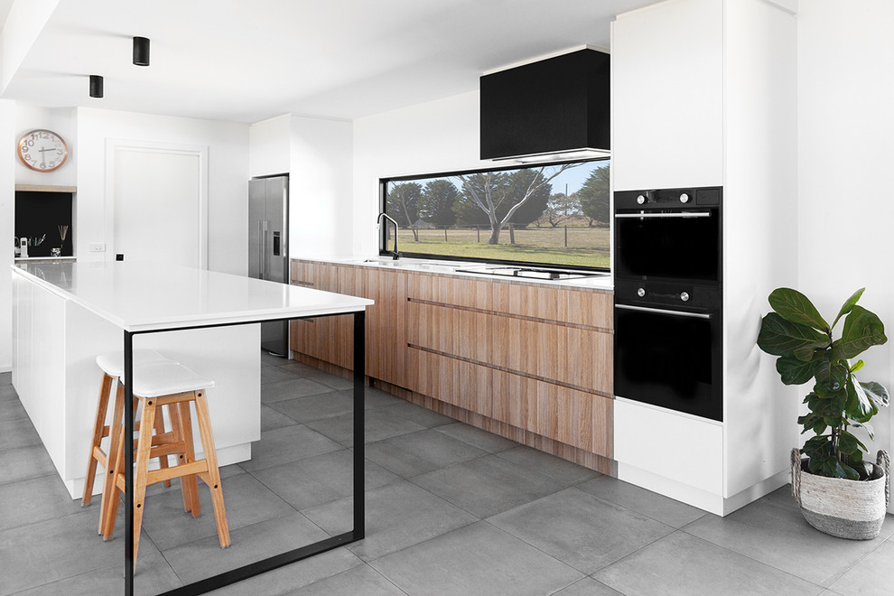 Photo of a mid-sized contemporary galley open plan kitchen in Geelong with with island, grey floor, medium wood cabinets, quartz benchtops, window splashback, black appliances, cement tiles and white benchtop.