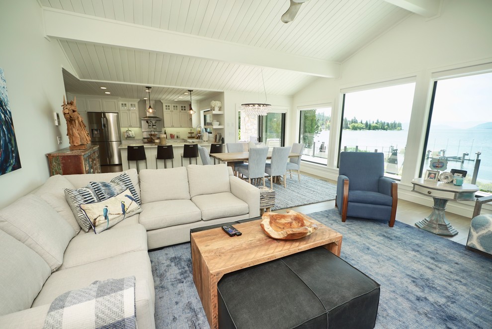 This is an example of a mid-sized beach style open concept family room with white walls, light hardwood floors, a standard fireplace, a plaster fireplace surround, a freestanding tv and brown floor.