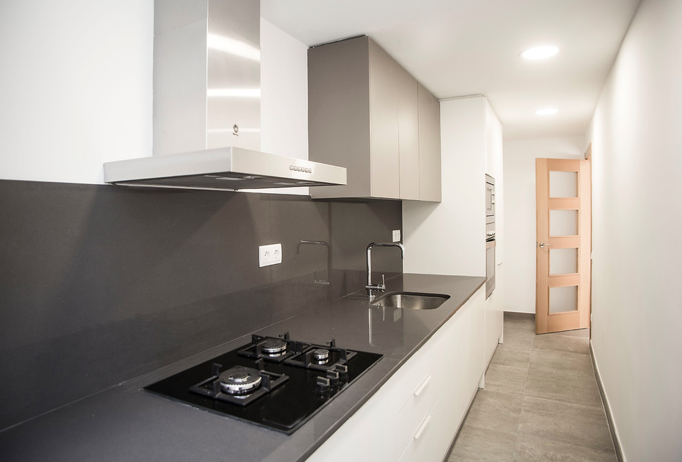 Photo of a mid-sized contemporary single-wall separate kitchen in Barcelona with a single-bowl sink, white cabinets, grey splashback, stainless steel appliances, no island and grey floor.