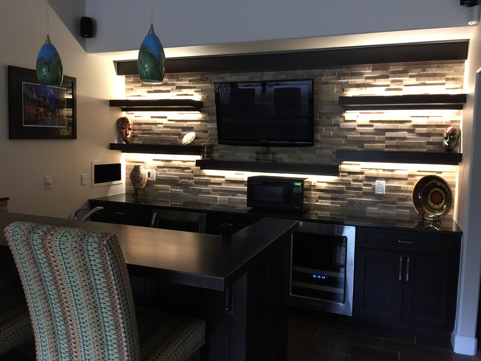 Photo of a mid-sized transitional galley seated home bar in Denver with an undermount sink, dark wood cabinets, grey splashback, stone tile splashback, porcelain floors and black benchtop.