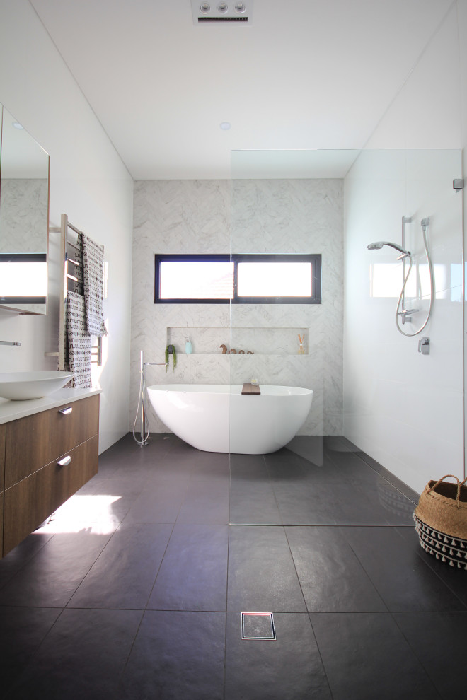 Photo of a mid-sized modern master wet room bathroom in Sydney with furniture-like cabinets, medium wood cabinets, a freestanding tub, a wall-mount toilet, white tile, porcelain tile, porcelain floors, a vessel sink, engineered quartz benchtops, grey floor and white benchtops.