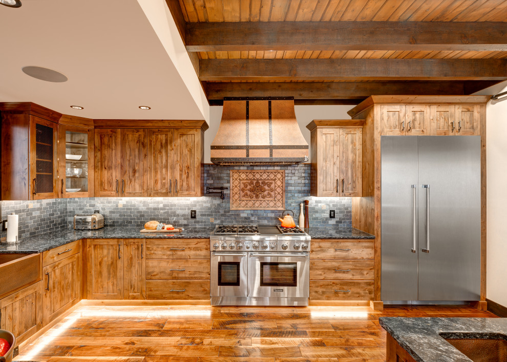 Design ideas for a country l-shaped kitchen in Vancouver with an undermount sink, shaker cabinets, medium wood cabinets, grey splashback, stainless steel appliances, medium hardwood floors, with island, brown floor, black benchtop, exposed beam and wood.