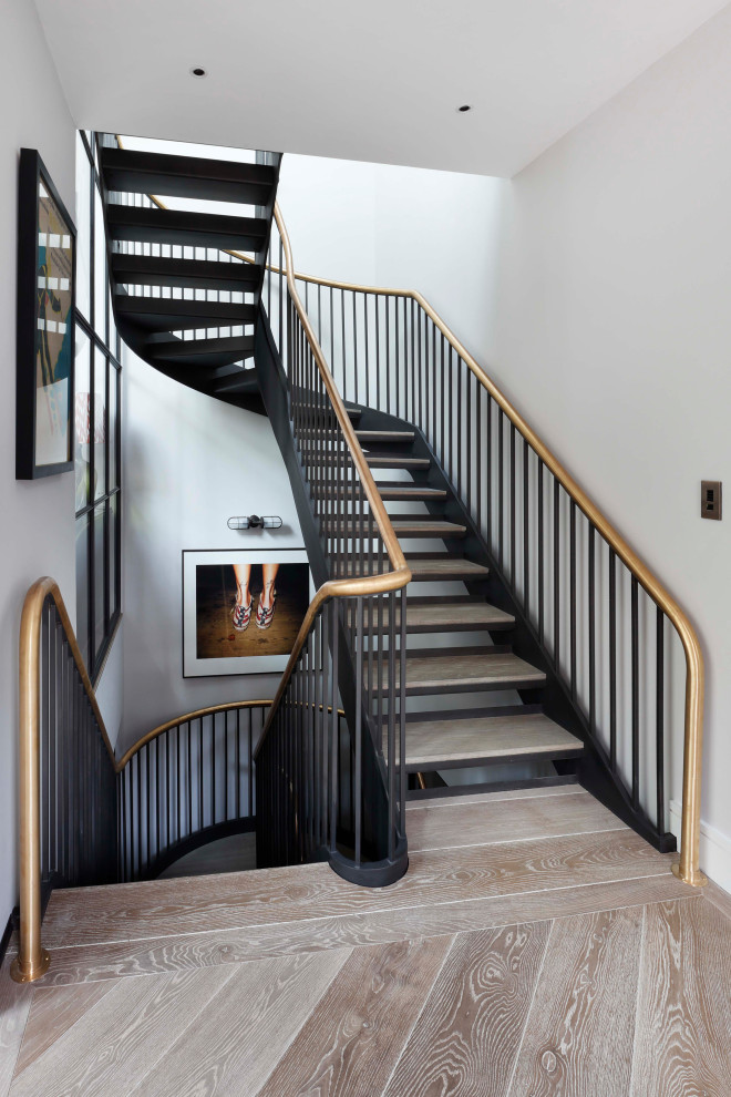 Large transitional wood curved staircase in London with open risers and metal railing.