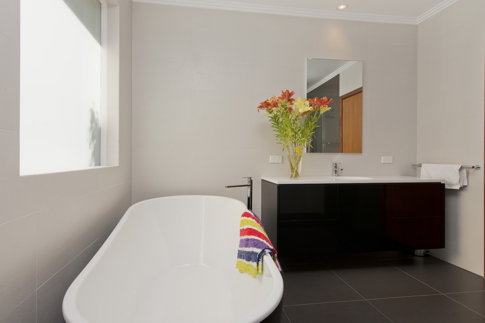 Mid-sized modern bathroom in Melbourne with flat-panel cabinets, black cabinets, a freestanding tub, an open shower, a wall-mount toilet, multi-coloured tile, porcelain tile, white walls, porcelain floors, an integrated sink, solid surface benchtops and grey floor.