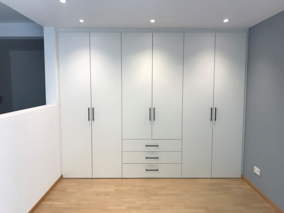 Design ideas for a mid-sized contemporary gender-neutral walk-in wardrobe in Paris with beaded inset cabinets, white cabinets and light hardwood floors.