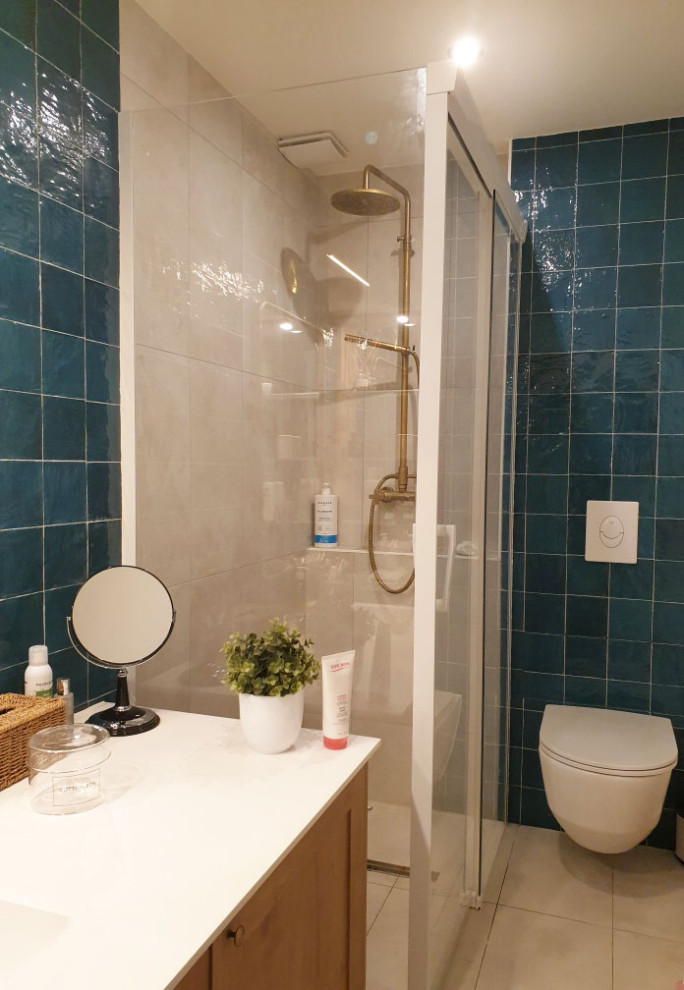 Klassisk inredning av ett litet vit vitt badrum med dusch, med luckor med lamellpanel, skåp i ljust trä, en kantlös dusch, en vägghängd toalettstol, blå kakel, mosaik, blå väggar, klinkergolv i keramik, ett undermonterad handfat, bänkskiva i akrylsten, beiget golv och dusch med skjutdörr