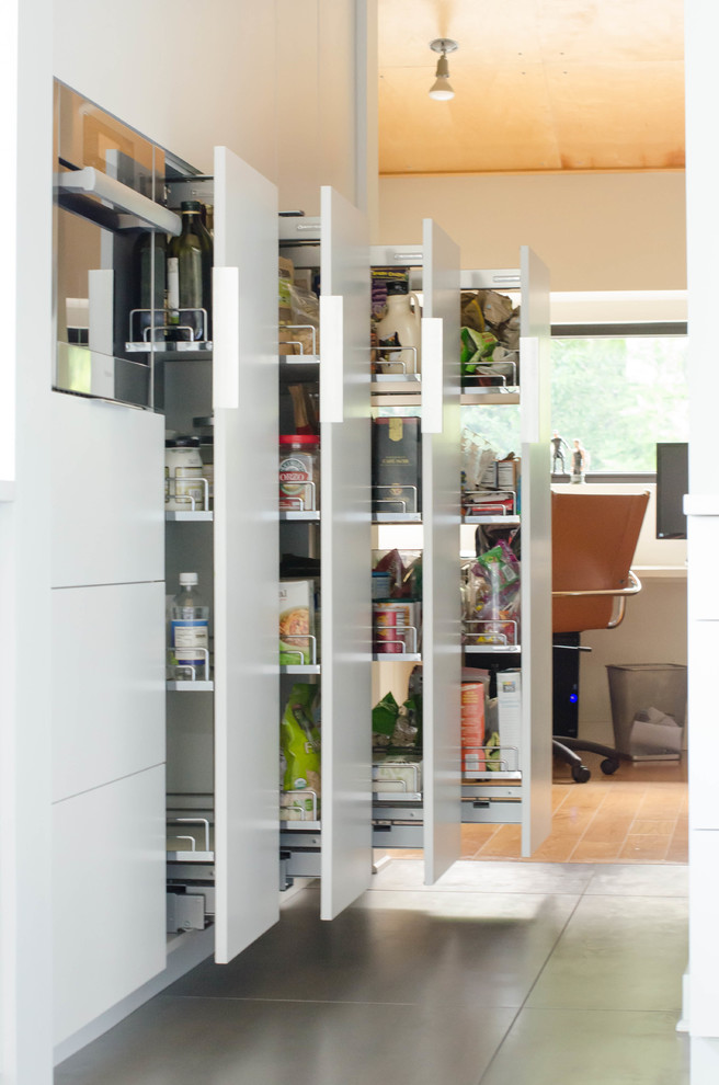This is an example of a large contemporary kitchen pantry in Kansas City with flat-panel cabinets, white cabinets, stainless steel appliances and porcelain floors.