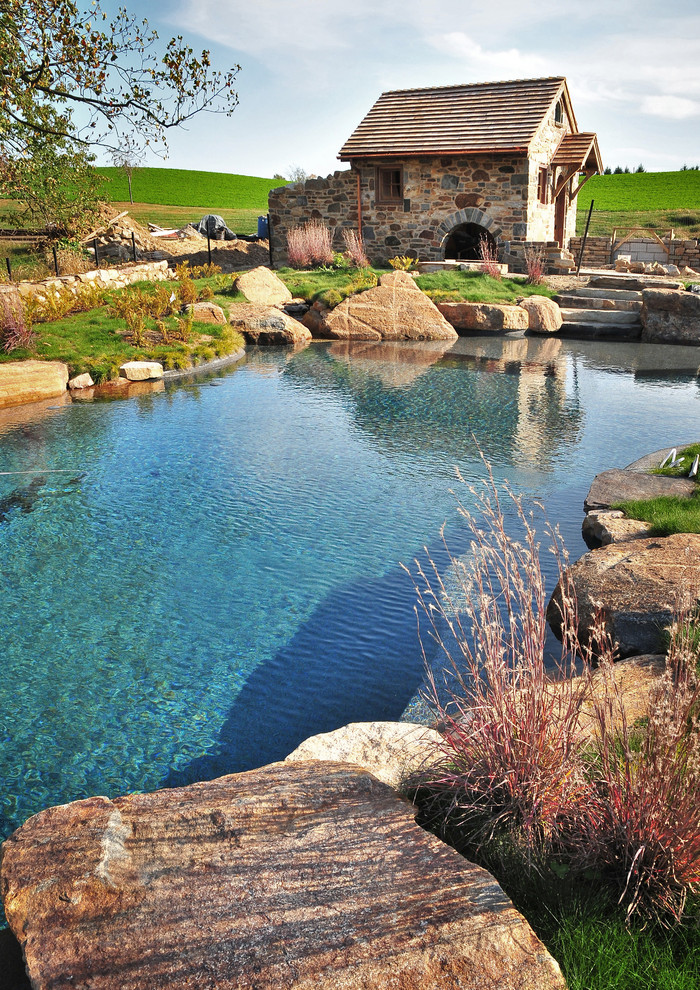 Design ideas for a large country backyard custom-shaped natural pool in Philadelphia with a pool house and natural stone pavers.