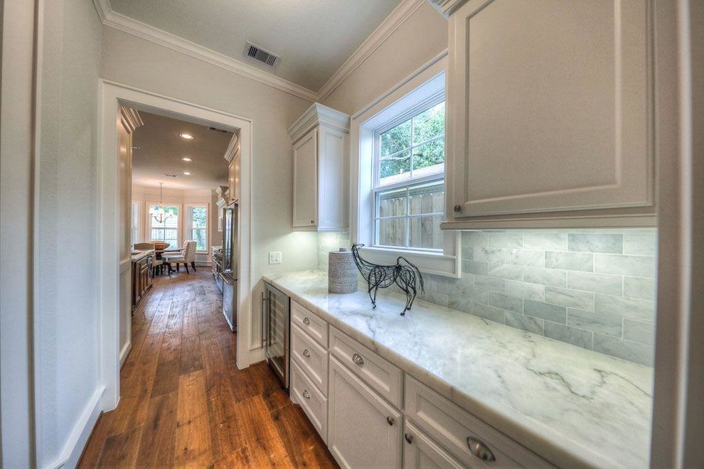 Open concept kitchen - large transitional medium tone wood floor open concept kitchen idea in Houston with a drop-in sink, shaker cabinets, white cabinets, quartzite countertops, gray backsplash, stone tile backsplash, stainless steel appliances and an island