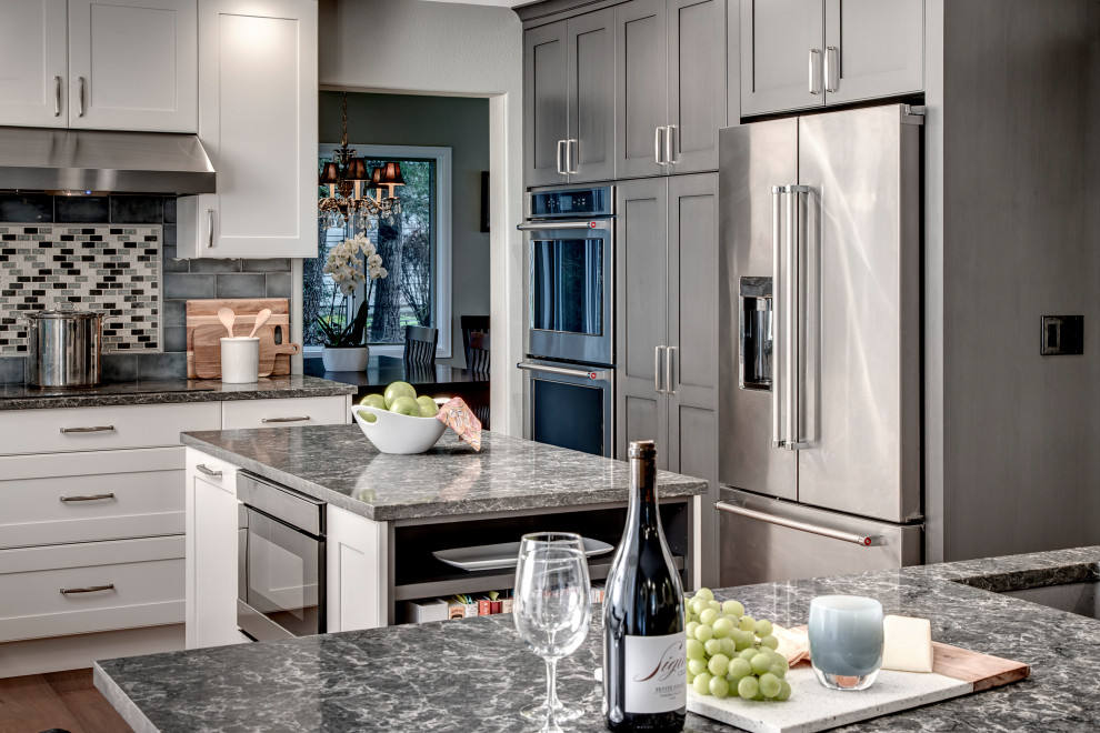 Example of a mid-sized transitional l-shaped medium tone wood floor and brown floor eat-in kitchen design in Seattle with a single-bowl sink, shaker cabinets, gray cabinets, quartz countertops, gray backsplash, ceramic backsplash, stainless steel appliances, two islands and gray countertops