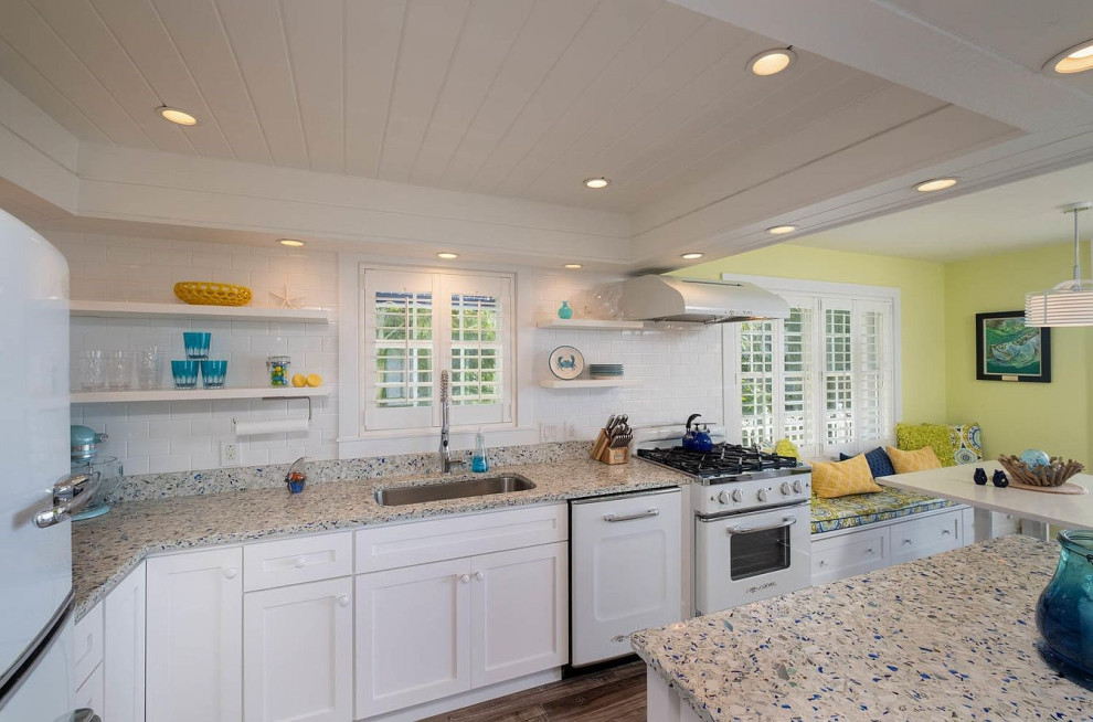 Mid-sized transitional u-shaped eat-in kitchen in Miami with an undermount sink, recessed-panel cabinets, white cabinets, granite benchtops, white splashback, subway tile splashback, white appliances, linoleum floors, with island, brown floor and multi-coloured benchtop.