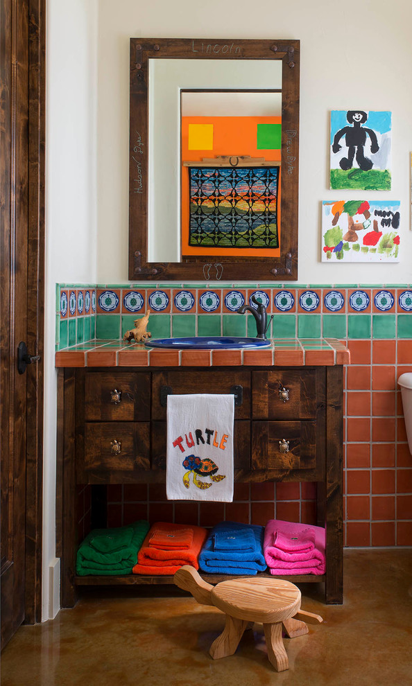This is an example of a kids bathroom in San Diego with dark wood cabinets, multi-coloured tile, terra-cotta tile, a drop-in sink, tile benchtops, white walls and flat-panel cabinets.