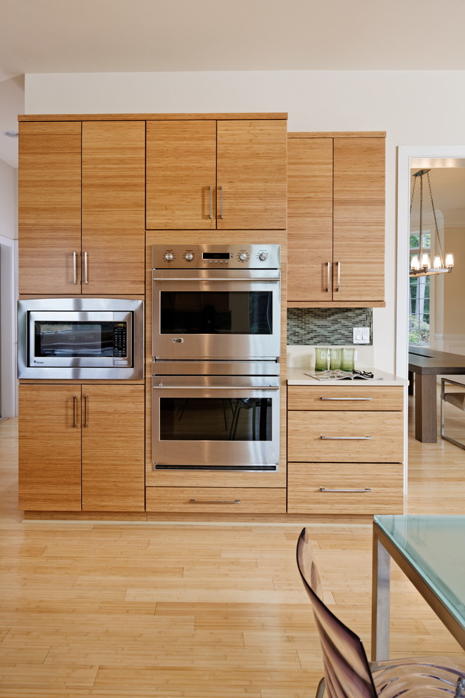 Inspiration for a contemporary kitchen in DC Metro with flat-panel cabinets, light wood cabinets, solid surface benchtops, green splashback, matchstick tile splashback, stainless steel appliances, bamboo floors, with island, beige floor and white benchtop.