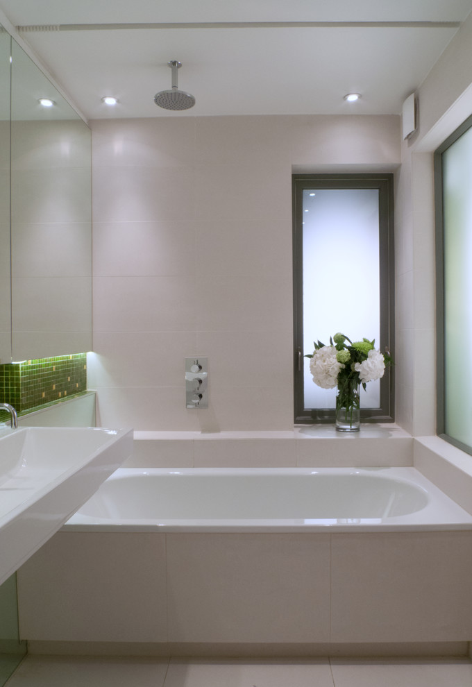 This is an example of a small contemporary kids bathroom in London with glass-front cabinets, white cabinets, a drop-in tub, a wall-mount toilet, green tile, mosaic tile, ceramic floors, a wall-mount sink and tile benchtops.