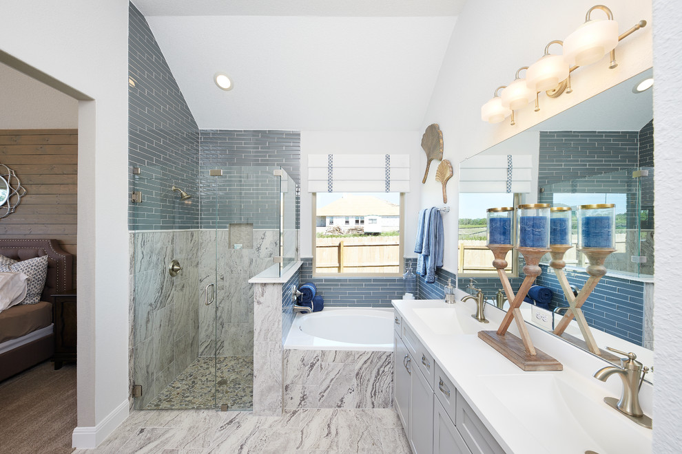Inspiration for a mid-sized transitional master bathroom in Austin with recessed-panel cabinets, grey cabinets, an undermount tub, a corner shower, blue tile, ceramic tile, white walls, ceramic floors, solid surface benchtops, a hinged shower door, white benchtops, an integrated sink and grey floor.