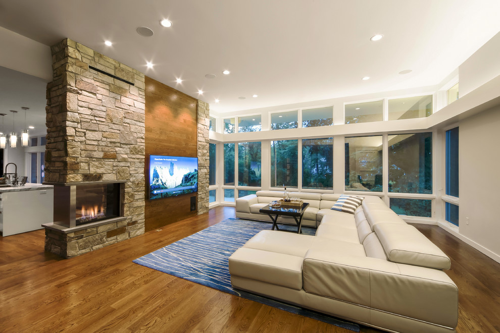 Design ideas for a large modern open concept family room in New York with brown walls, dark hardwood floors, a two-sided fireplace, a stone fireplace surround, a wall-mounted tv and brown floor.