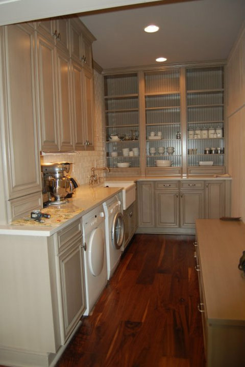 Inspiration for a mid-sized timeless l-shaped dark wood floor and brown floor utility room remodel in Huntington with a farmhouse sink, raised-panel cabinets, beige cabinets, granite countertops, white walls and a side-by-side washer/dryer