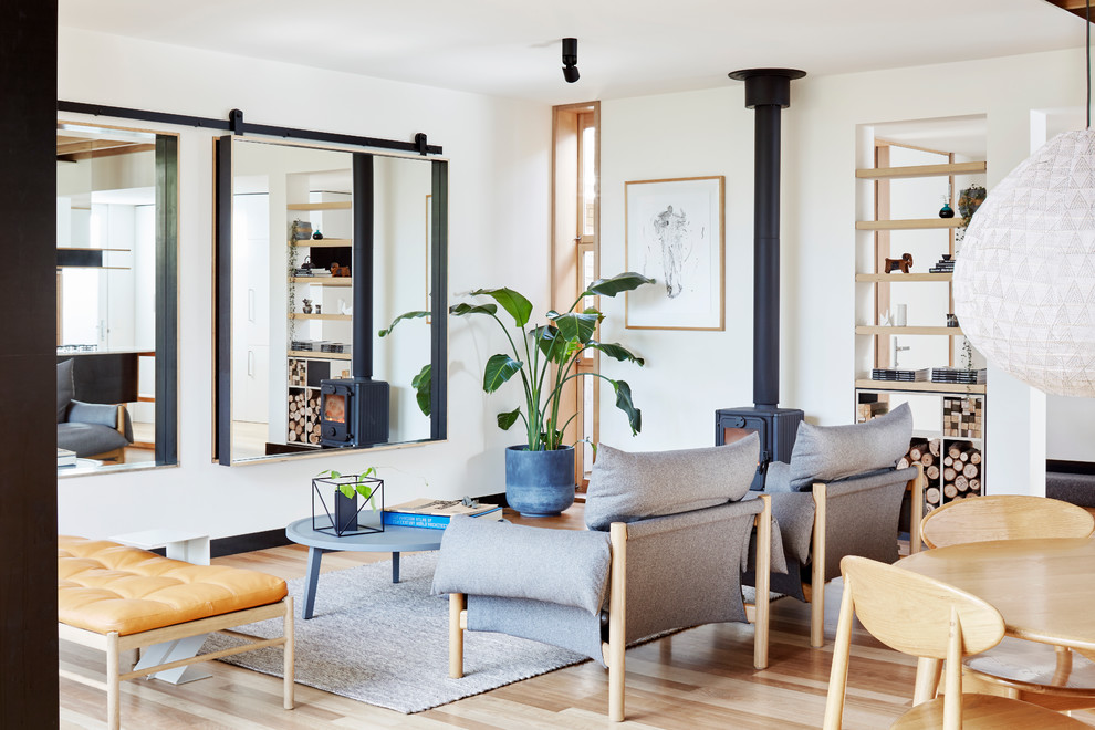 This is an example of a small contemporary open concept living room in Melbourne with white walls, light hardwood floors, a wood stove and a concealed tv.