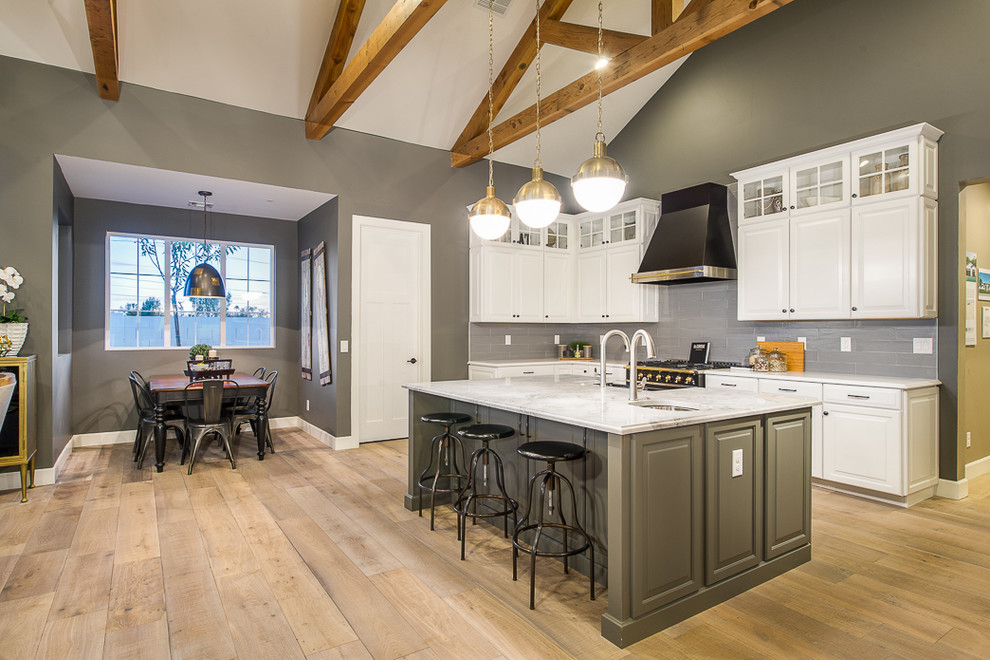 This is an example of a large transitional open plan kitchen in Phoenix with a farmhouse sink, raised-panel cabinets, white cabinets, grey splashback, glass tile splashback, stainless steel appliances, light hardwood floors and with island.