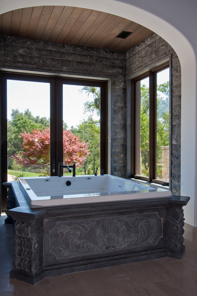 This is an example of a large mediterranean master bathroom in Sacramento with a hot tub, gray tile, stone tile, grey walls and limestone floors.