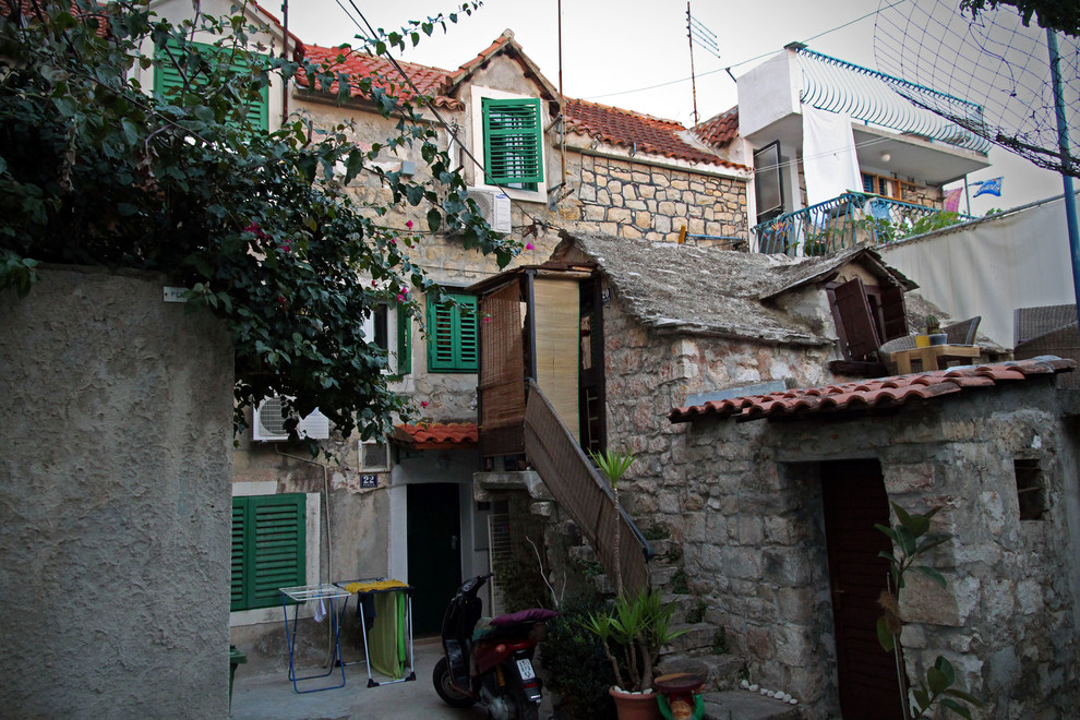 Photo of a small mediterranean three-storey exterior in Other with stone veneer and a gable roof.