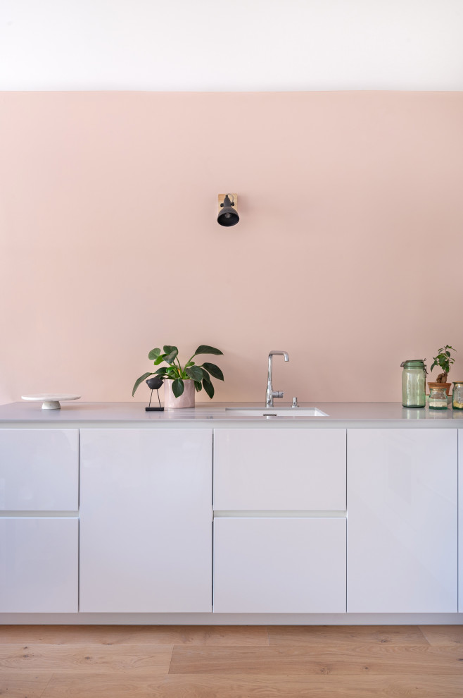 Idéer för ett stort modernt grå kök, med en integrerad diskho, släta luckor, vita skåp, rosa stänkskydd, stänkskydd i keramik, integrerade vitvaror och ljust trägolv
