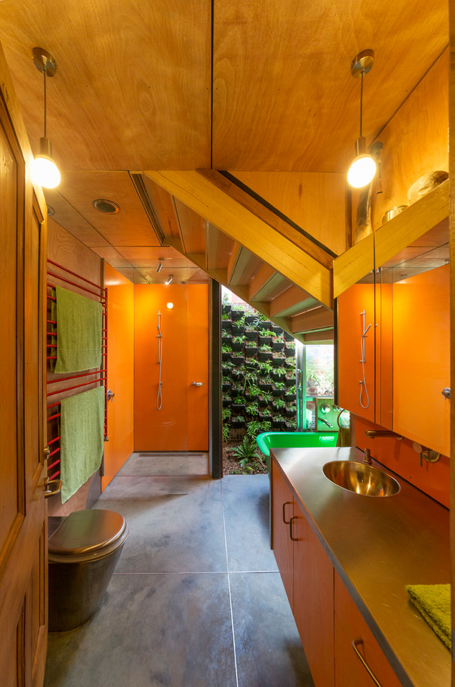 Industrial bathroom in Melbourne with an integrated sink, flat-panel cabinets, medium wood cabinets, a freestanding tub, an open shower, orange tile, orange walls and an open shower.