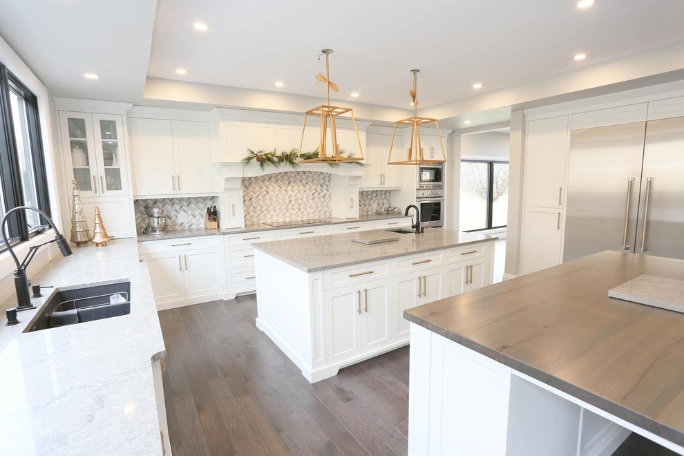 Enclosed kitchen - large transitional u-shaped dark wood floor and brown floor enclosed kitchen idea with an undermount sink, shaker cabinets, white cabinets, granite countertops, gray backsplash, mosaic tile backsplash, stainless steel appliances, two islands and gray countertops