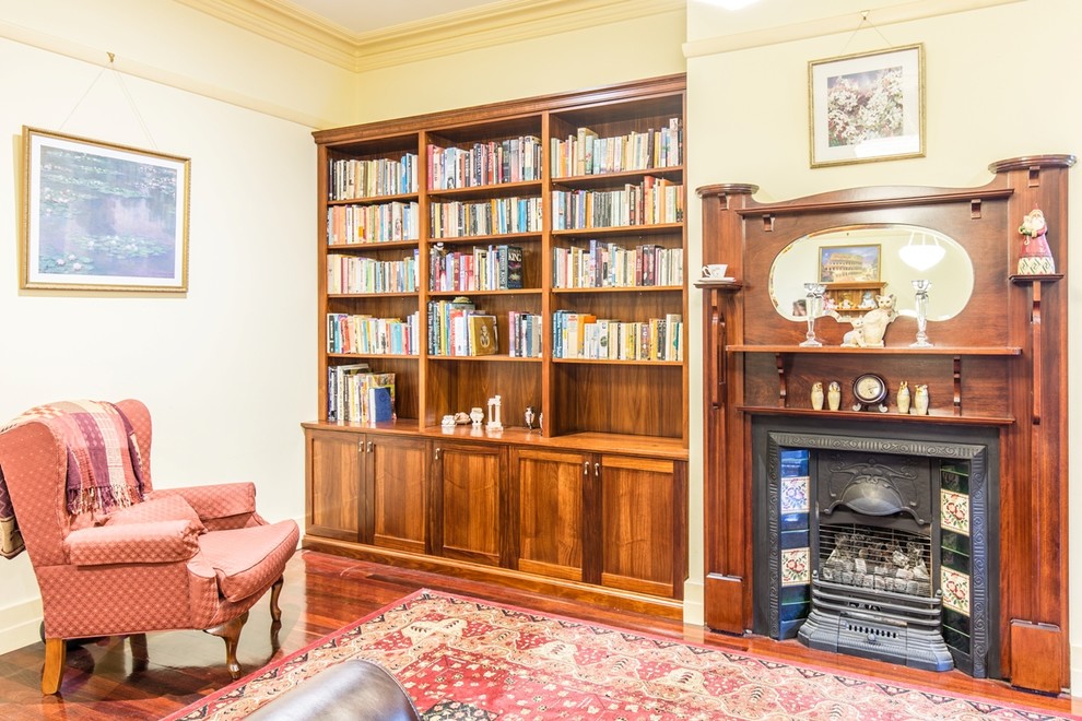 Photo of a mid-sized traditional enclosed living room in Melbourne with a library, yellow walls, dark hardwood floors, a standard fireplace, a wood fireplace surround and no tv.