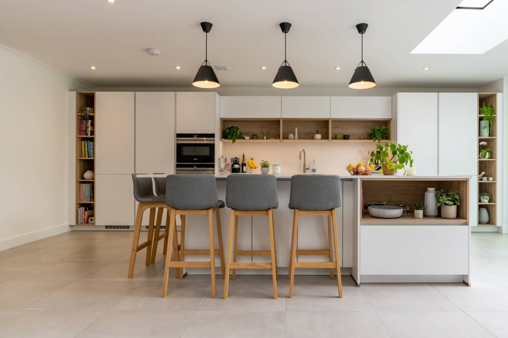 This is an example of a large scandi galley open plan kitchen in Hertfordshire with flat-panel cabinets, white cabinets, quartz worktops, white splashback, black appliances, an island, white floors, white worktops and feature lighting.