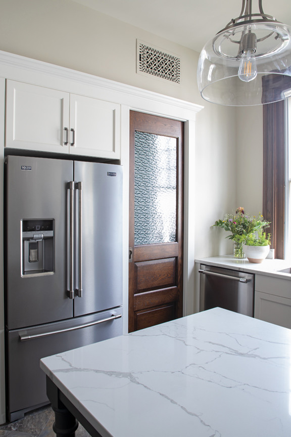 Transitional l-shaped kitchen photo with an undermount sink, quartz countertops, white backsplash, stone slab backsplash, stainless steel appliances, an island and white countertops