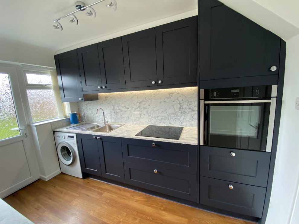This is an example of a mid-sized modern open plan kitchen in Other with an undermount sink, shaker cabinets, grey cabinets, laminate benchtops, white splashback, black appliances, vinyl floors, with island, brown floor and white benchtop.