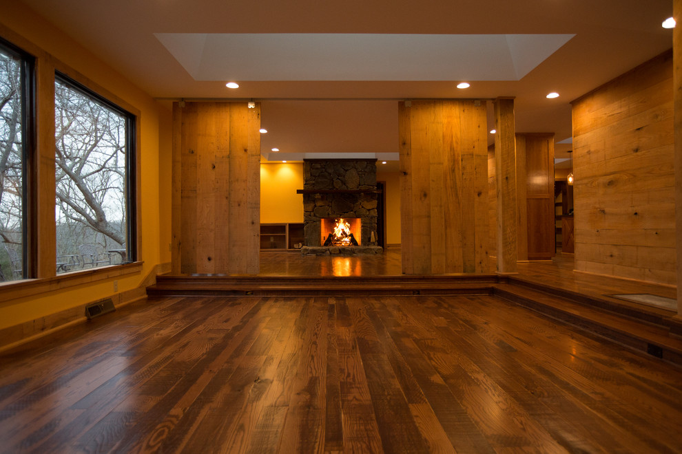 Large mountain style formal and open concept dark wood floor home design photo with orange walls, a standard fireplace, a stone fireplace and no tv