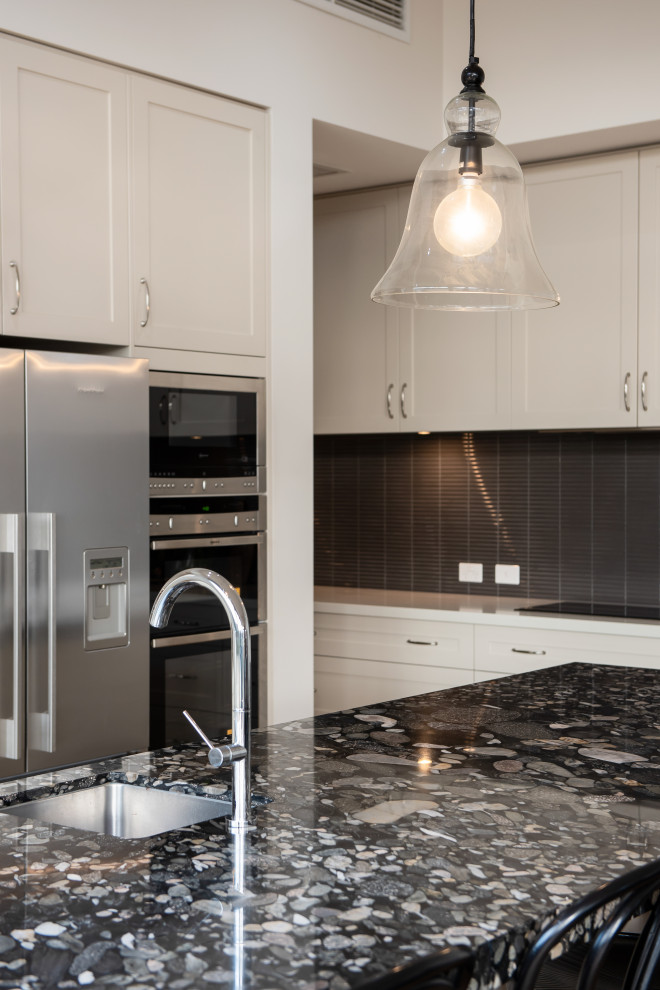 This is an example of an expansive transitional l-shaped open plan kitchen in Geelong with an undermount sink, shaker cabinets, white cabinets, matchstick tile splashback, stainless steel appliances, dark hardwood floors, with island, black benchtop, granite benchtops and grey splashback.