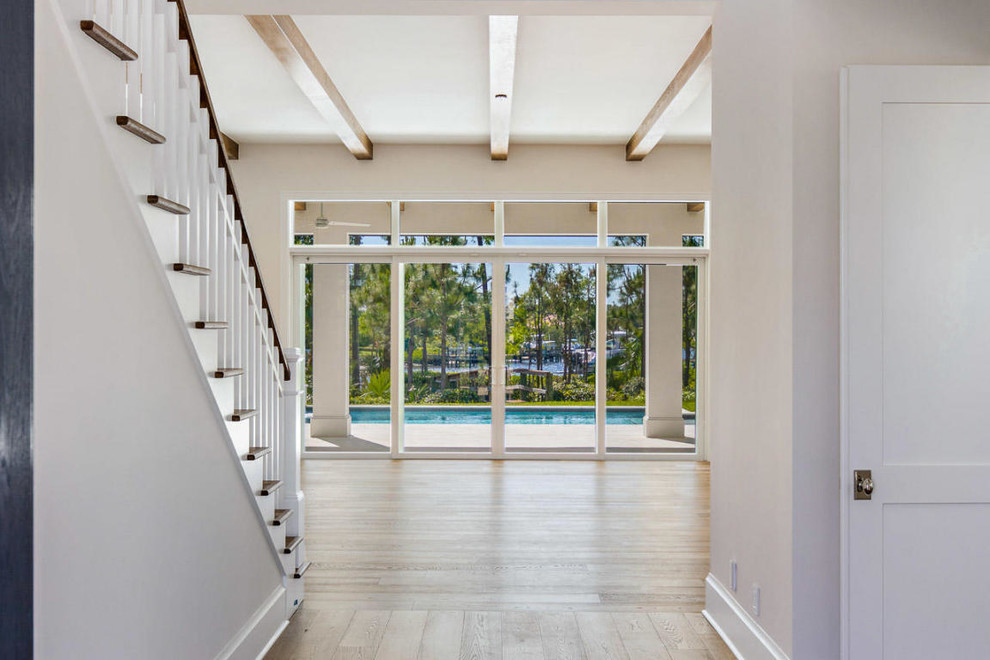 This is an example of a large beach style entryway in Miami with white walls, medium hardwood floors, brown floor and exposed beam.