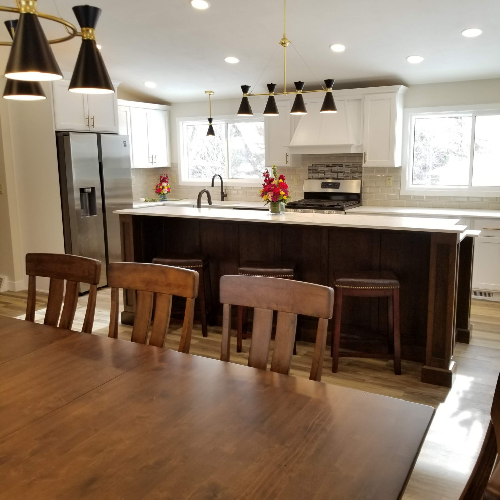 Photo of a large traditional l-shaped kitchen/diner in Milwaukee with a submerged sink, shaker cabinets, white cabinets, white splashback, porcelain splashback, vinyl flooring, an island, brown floors, white worktops and a vaulted ceiling.