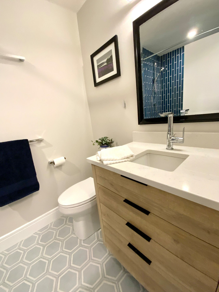 Photo of a small rural family bathroom in Calgary with flat-panel cabinets, light wood cabinets, an alcove bath, a shower/bath combination, a one-piece toilet, blue tiles, ceramic tiles, white walls, ceramic flooring, a submerged sink, quartz worktops, blue floors, an open shower, white worktops, a single sink and a built in vanity unit.